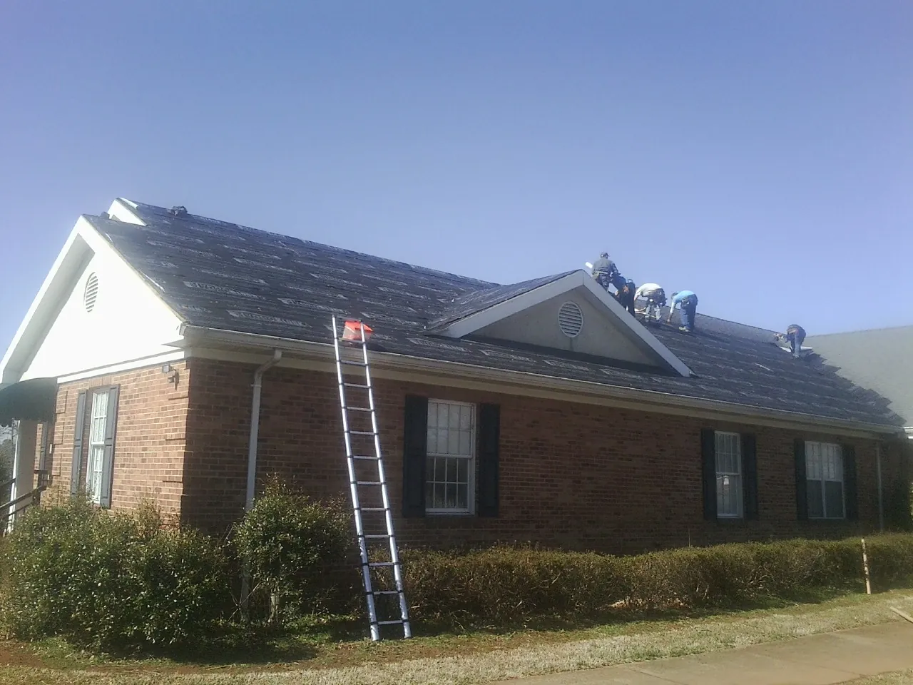Crew tearing shingles off a brick ranch roof with a ladder set — Metal Roof Repair work by our crew in Eden