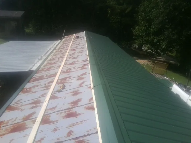 Old rusted panels beside newly installed green metal roofing — Wind Damage Roof Repair by Roofing Brothers in Eden