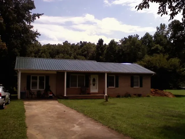 Dark green metal roof on a brick ranch with a covered porch in Eden